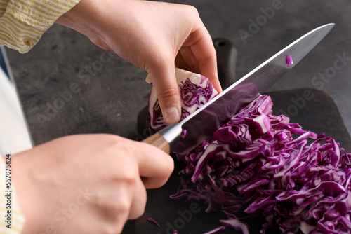 Woman cutting fresh red cabbage at black table, closeup