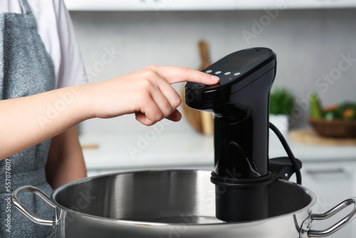 Woman using thermal immersion circulator in kitchen, closeup. Sous vide cooking photo