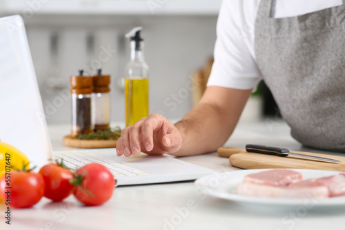 Man making dinner while watching online cooking course via laptop in kitchen, closeup