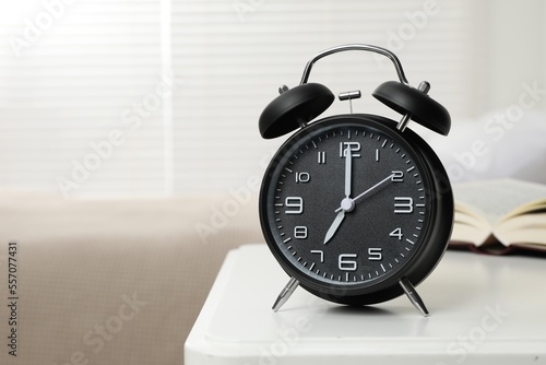 Black alarm clock on white wooden nightstand in bedroom, space for text