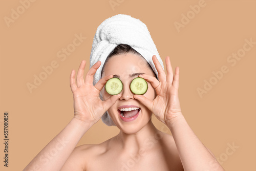 Woman with towel holding pieces of cucumber on beige background. Spa treatment