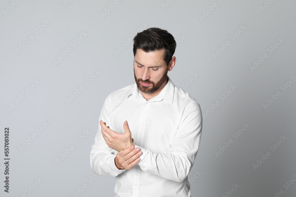 Man suffering from pain in his hand on light background. Arthritis symptoms