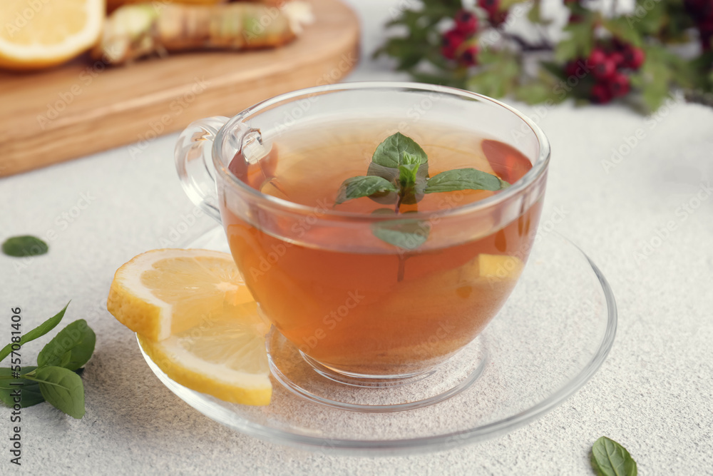 Glass cup of delicious immunity boosting tea with ingredients on light grey table, closeup Glass cup of delicious immunity boosting tea with ingredients on light grey table, closeup