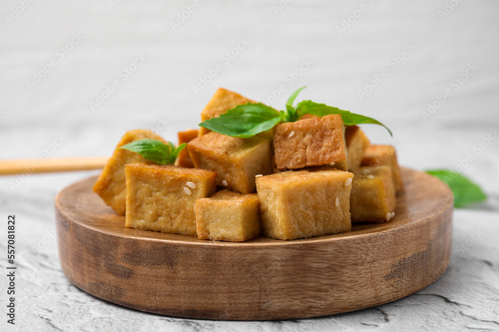 Wooden plate with delicious fried tofu, basil and sesame seeds on light grey table