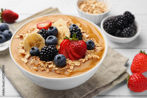 Delicious smoothie bowl with fresh berries, banana and oatmeal on white wooden table, closeup