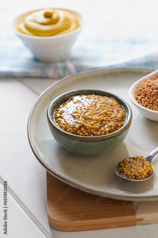 Bowl and spoon of whole grain mustard on white wooden table Bowl and spoon of whole grain mustard on white wooden table