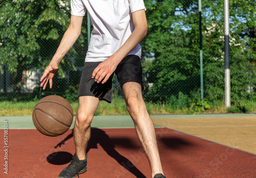 Cute young teenager in t shirt with a ball plays basketball on court. Teenager running in the stadium. Sports, hobby, active lifestyle for boys