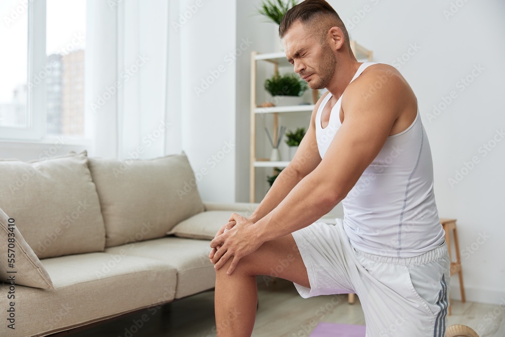 Man sports pain in the side and leg during a workout at home, pumped up man sports, the concept of health without injuries and sprains muscles and ligaments of the body Man sports pain in the side and leg during a workout at home, pumped up man sports, the concept of health without injuries and sprains muscles and ligaments of the body