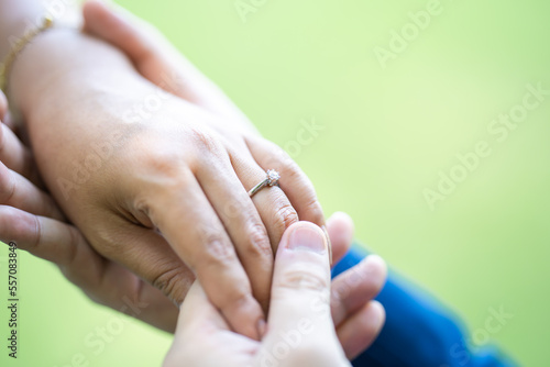 A man is wearing a wedding ring to a woman on his left ring finger. Close up on the hand in the outdoor field with the sunlight and tree shadow shading.