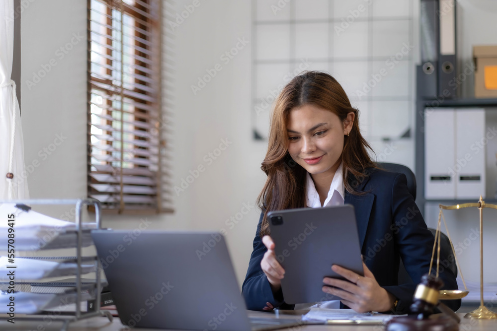 © wichayada - Attractive young lawyer in office Business woman and lawyers discussing contract papers with brass scale on wooden desk in office. Law, legal services, advice, Justice and real estate concept.