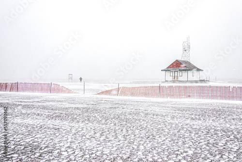 As a snow storm blows a lone figure walks on an empty beach by a wooden lifeguard station.  Shot in Toronto s beaches neighbourhood.  Room for text.