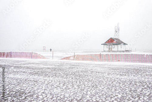 Photography As a snow storm blows a lone figure walks on an empty beach by a wooden lifeguard station