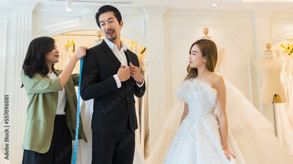 Bride and groom wear dress and try to fitting in modern wedding studio with bridal store owner 