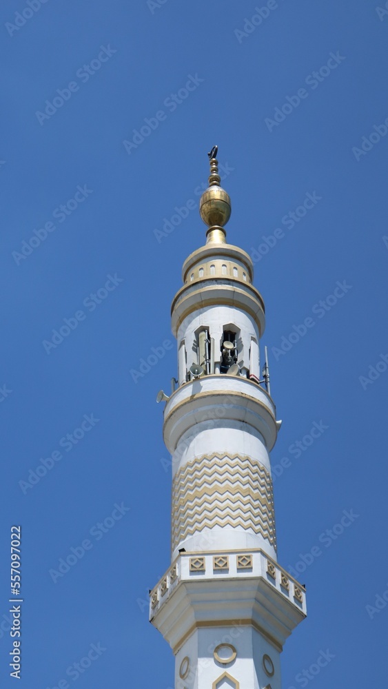Low angle view Single Minaret of Muslim mosque on the clear blue sky background. Islam, religion and architecture, and travel concept. Mosque design in Islamic religious architectural traditions.