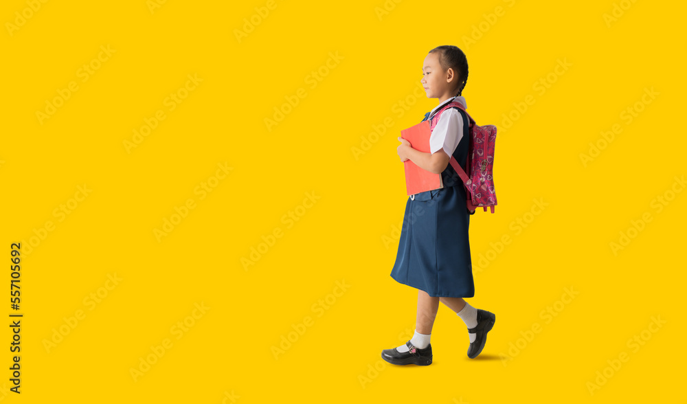 Fototapeta premium Asian student child girl wears school uniform holding book with walking back to school, isolated on yellow background