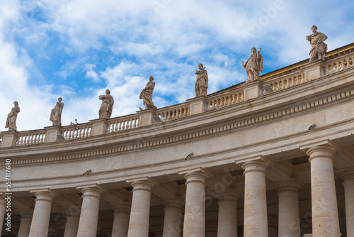 Colonnade with statues of saints made of marble in the famous "Piazza San Pietro" (Saint Peter Square) in Vatican city, Rome, Italy. Blue sky with white clouds on the background.