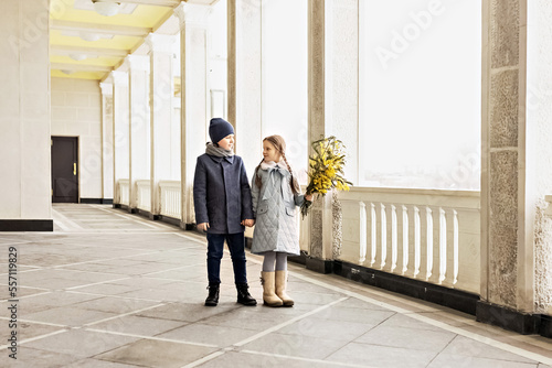 Portrait of a couple of a boy and a girl of schoolchildren in spring coats with a bouquet of mimosa in their hands in the park. Spring, International Women's Day on March 8. © Светлана Густова