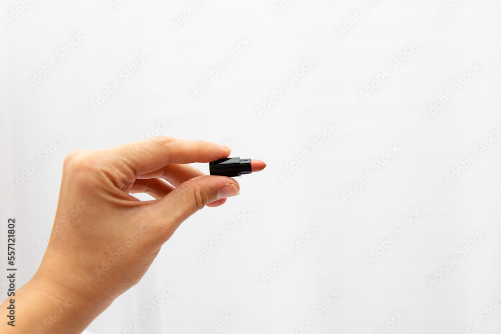 A woman's hand holds a lipstick miniature on a white background. Natural color lipstick sampler A woman's hand holds a lipstick miniature on a white background. Natural color lipstick sampler