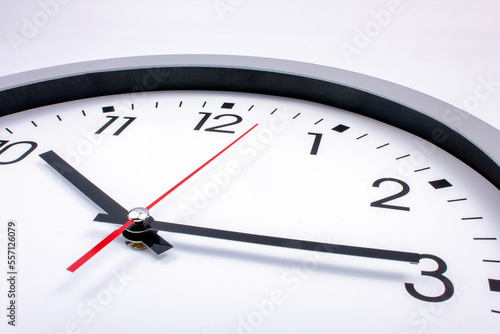 Black and white office clock with a red pointer on a gray background.