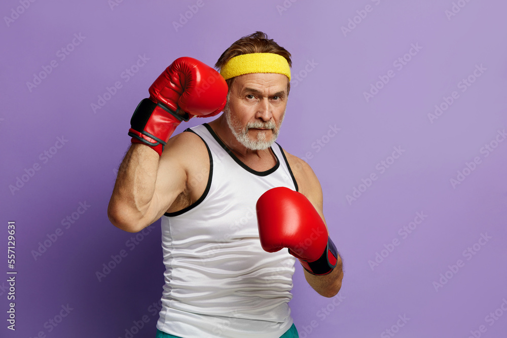 Strong Man Boxing In Gloves. Portrait of Senior Man Training And Demonstrating Power in His Hands, Feeling Energy In His Age. Indoor Studio Shot Isolated on Violet Background Strong Man Boxing In Gloves. Portrait of Senior Man Training And Demonstrating Power in His Hands, Feeling Energy In His Age. Indoor Studio Shot Isolated on Violet Background