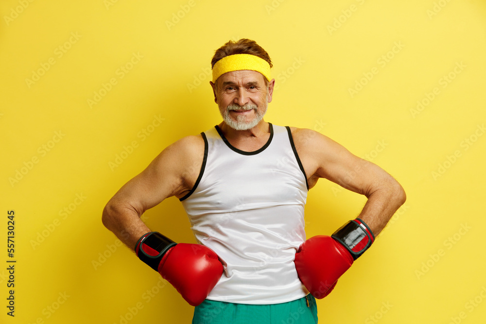 Strong Man Boxing In Gloves. Portrait of Senior Man Training And Demonstrating Power in His Hands, Feeling Energy In His Age. Indoor Studio Shot Isolated on Yellow Background 