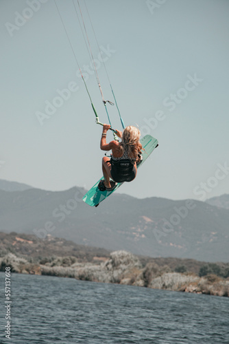 Female kitesurfer in full jump performing an artistic and extreme figure with her board above the water of the Mediterranean Sea in Corsica near Propriano 