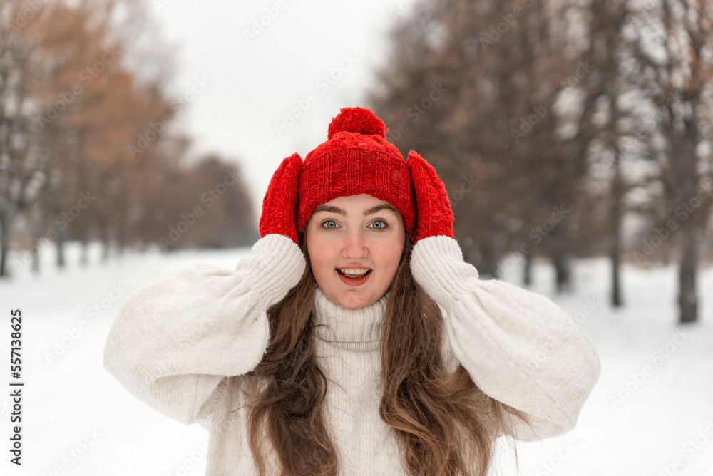 Portrait of joyful beautiful young woman in white wool sweater, red hat and mittens in winter park.Woman in warm clothes Portrait of joyful beautiful young woman in white wool sweater, red hat and mittens in winter park.Woman in warm clothes