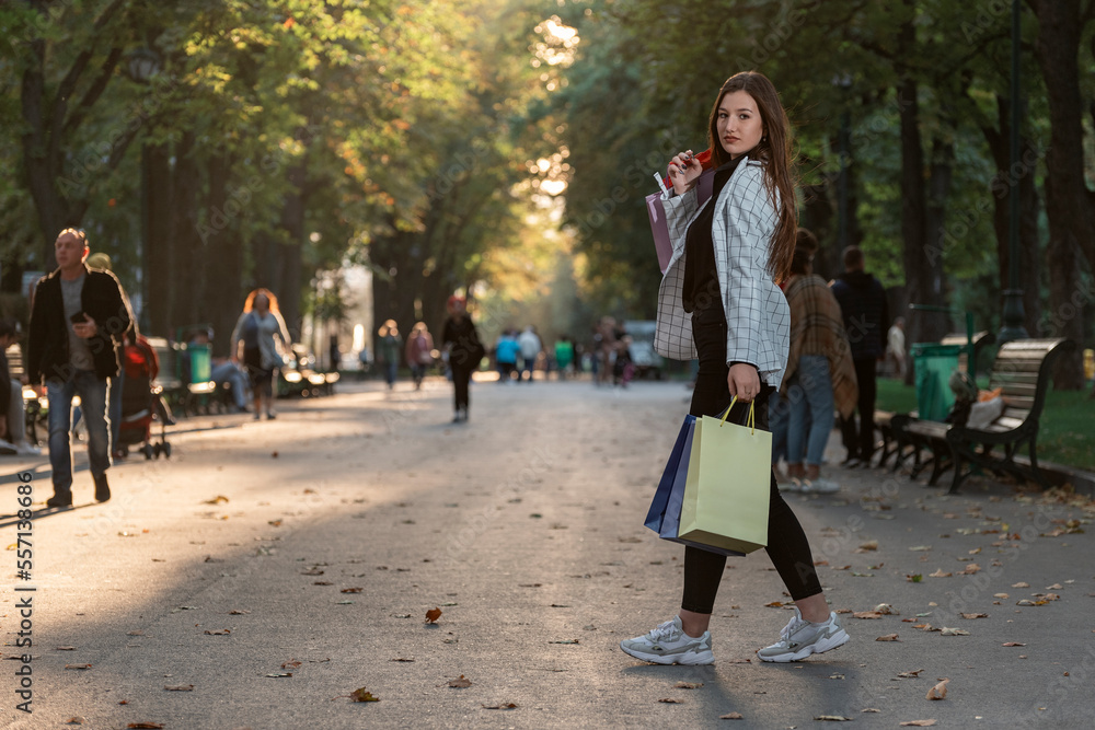 Full-length portrait of young woman with paper shopping bags walking in park. Happy customer. Full-length portrait of young woman with paper shopping bags walking in park. Happy customer.