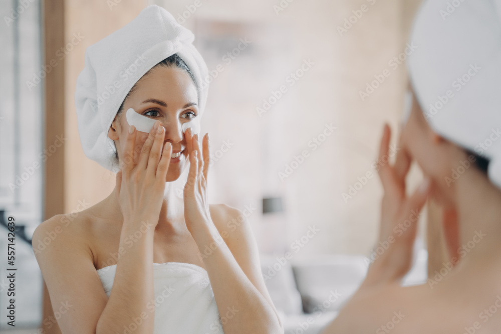 Girl applies eye patches and looking into mirror. Attractive woman wrapped in towel after bathing. Girl applies eye patches and looking into mirror. Attractive woman wrapped in towel after bathing.