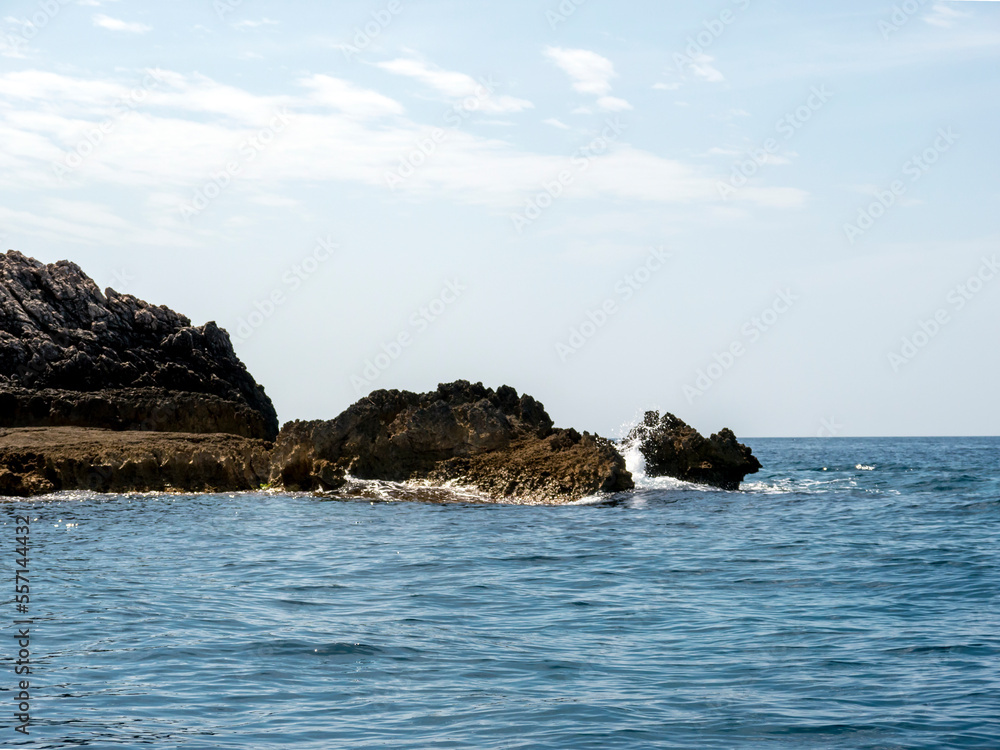 Massive rock pices in sea with white wave foam under clear blue sky