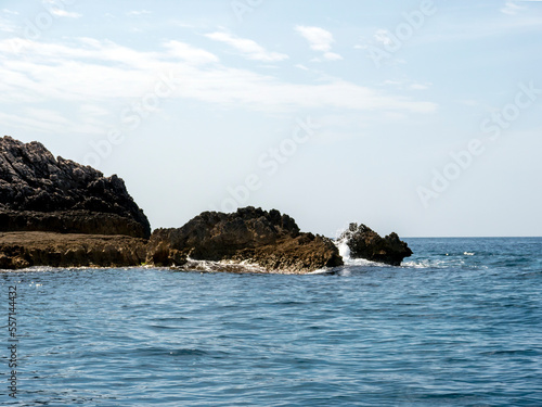 Massive rock pices in sea with white wave foam under clear blue sky