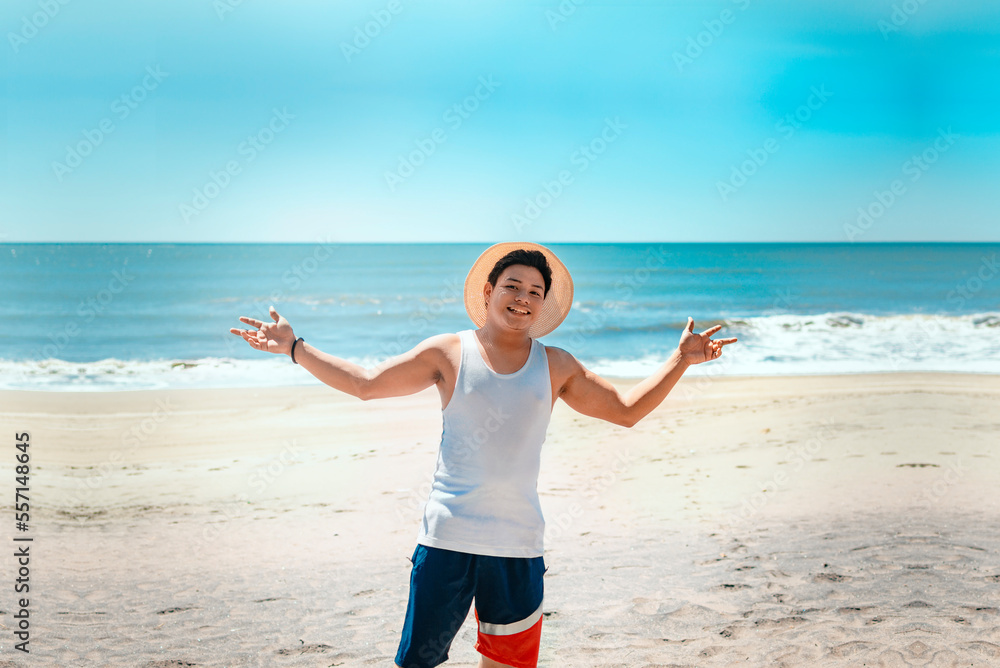 Concept of man enjoying the beach. Portrait of man in hat on the beach spreading his arms. Smiling young man on the beach spreading arms looking at camera Concept of man enjoying the beach. Portrait of man in hat on the beach spreading his arms. Smiling young man on the beach spreading arms looking at camera