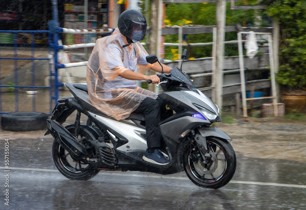 A man in a raincoat rides a motorcycle on the street in heavy rain