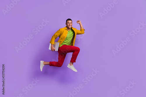 Full body profile photo of crazy active person hold netbook jump hurry rush empty space isolated on violet color background