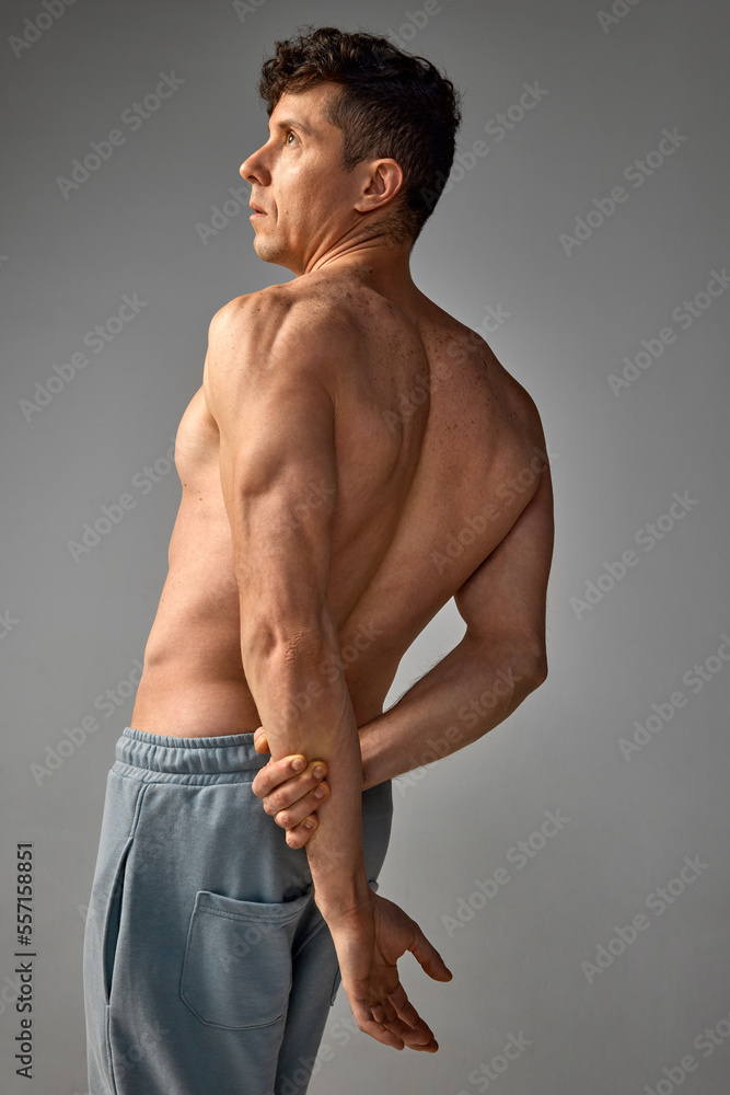 Strong, muscular, relief body shape. Mature handsome man posing shirtless, in pants over grey studio background. Men's health and beauty