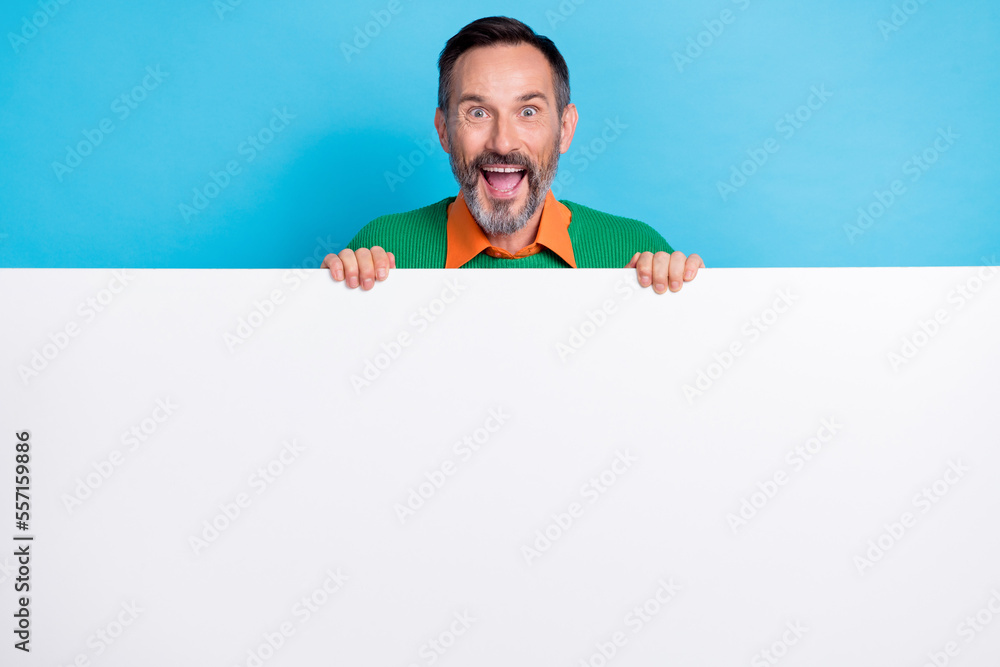Photo portrait of mature attractive male hiding behind white blank white wall dressed stylish green look isolated on blue color background Photo portrait of mature attractive male hiding behind white blank white wall dressed stylish green look isolated on blue color background