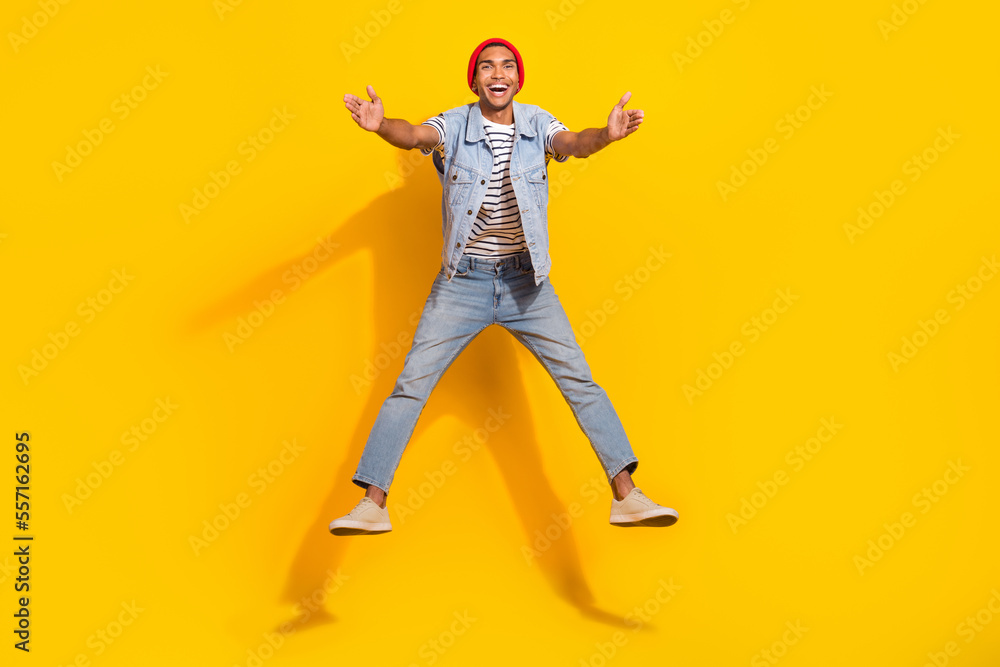 Full length photo of excited charming man wear jeans outfit jumping high ready hug you isolated yellow color background Full length photo of excited charming man wear jeans outfit jumping high ready hug you isolated yellow color background