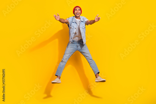 Full length photo of excited charming man wear jeans outfit jumping high ready hug you isolated yellow color background