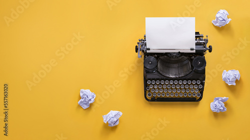 Vintage typewriter and crumpled papers over yellow background with copy space photo