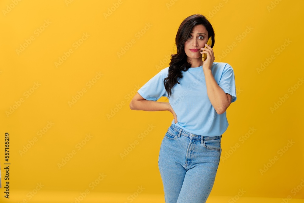 Woman blogger with a phone in her hands in a blue t-shirt and jeans on a yellow background smile signs gestures symbols, online communication and video call, copy space, free background Woman blogger with a phone in her hands in a blue t-shirt and jeans on a yellow background smile signs gestures symbols, online communication and video call, copy space, free background