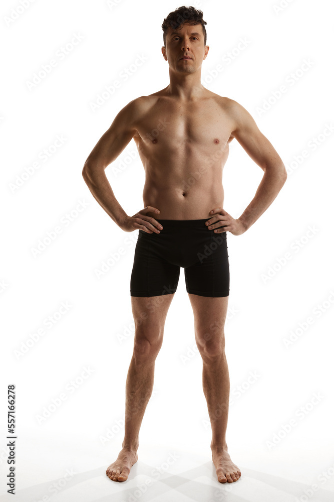 Front view. Portrait of mature handsome man with muscular body posing shirtless in black boxers over white studio background. Men's health and beauty