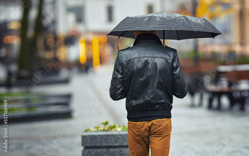 Alone man with umbrella. Man with umbrella walk on city street on rainy day. Back view of stylish man in rainy weather.