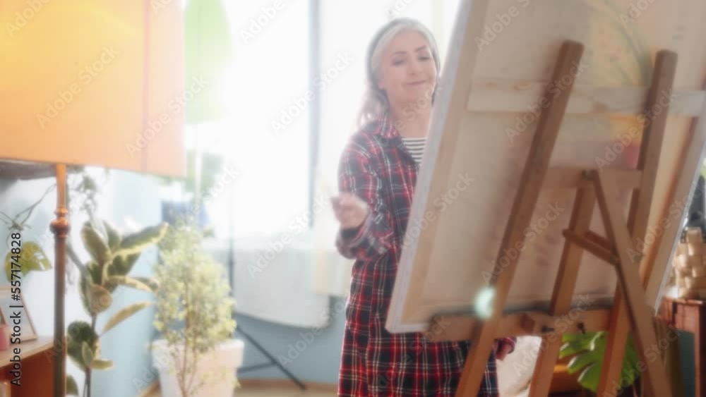 Portrait of charming senior woman artist painting picture on canvas creating artwork in the light sunny creative workshop Stylish mature grey haired lady enjoying leisure time with art hobby indoors Portrait of charming senior woman artist painting picture on canvas creating artwork in the light sunny creative workshop Stylish mature grey haired lady enjoying leisure time with art hobby indoors