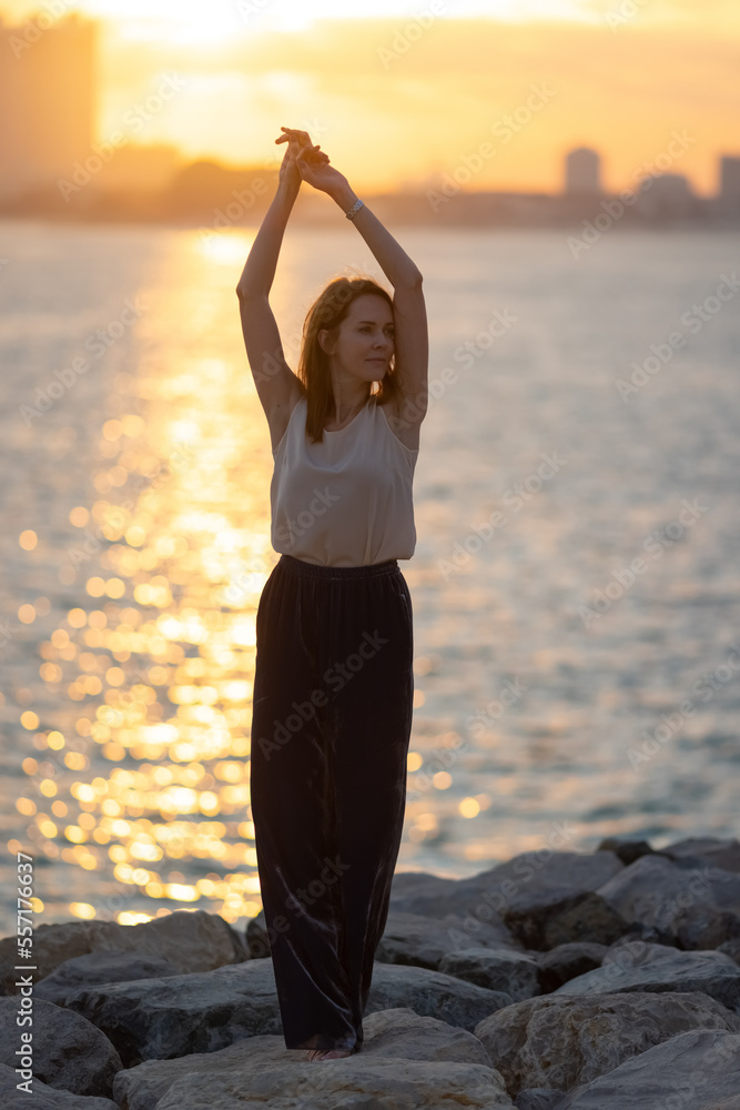 Woman practicing yoga meditation at sunrise. Morning yoga on the beach or coast of sea urban city background.