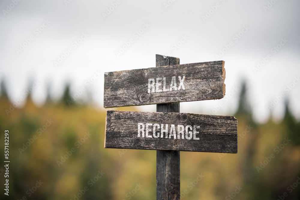 vintage and rustic wooden signpost with the weathered text quote relax recharge, outdoors in nature. blurred out forest fall colors in the background.