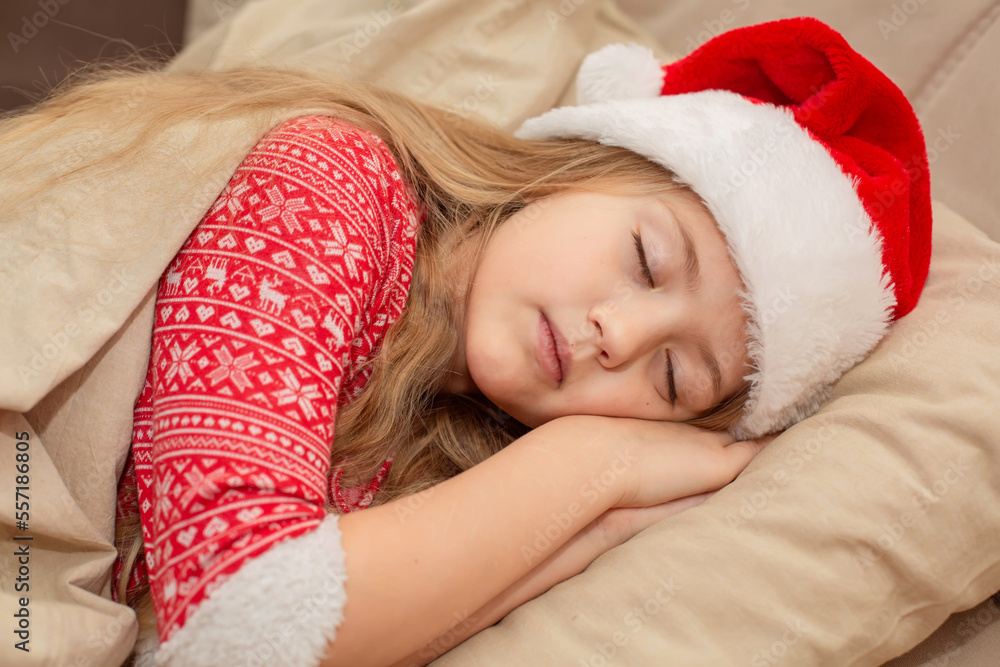 a beautiful blonde girl in a Santa Claus hat and New Year's pajamas is sleeping in bed