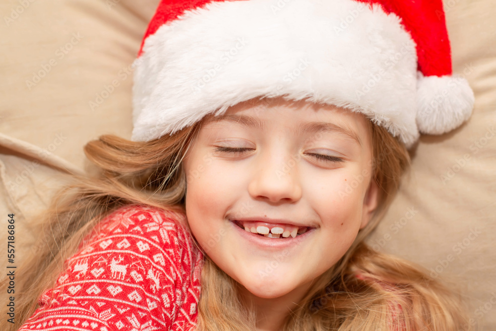 a happy blonde girl in a Santa Claus hat and New Year's pajamas is lying in bed a happy blonde girl in a Santa Claus hat and New Year's pajamas is lying in bed