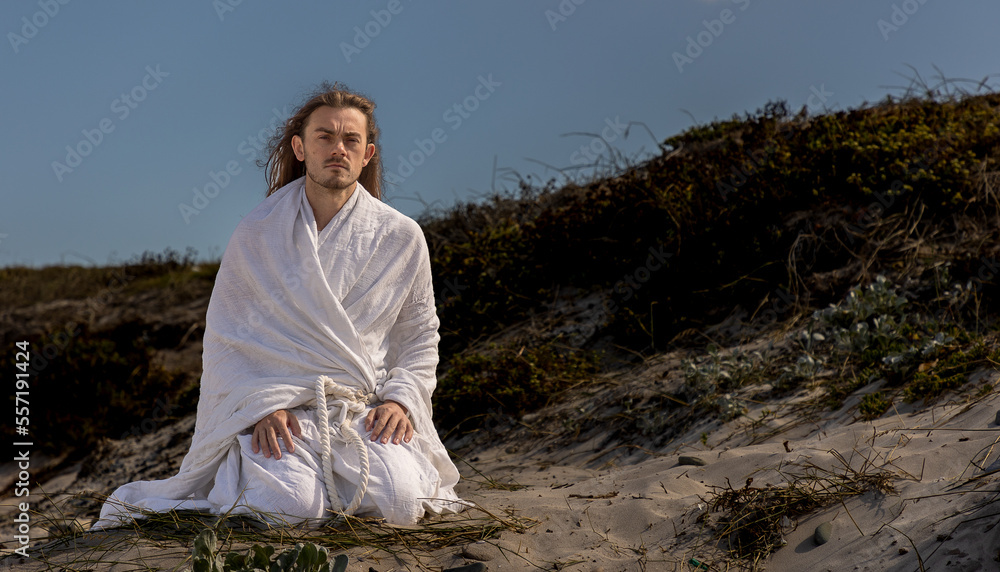 biblical man in white robe kneels in prayer in desert