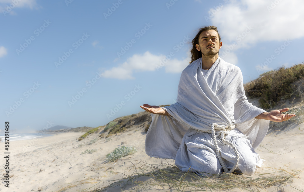 praying man in white robe in desert with arms open