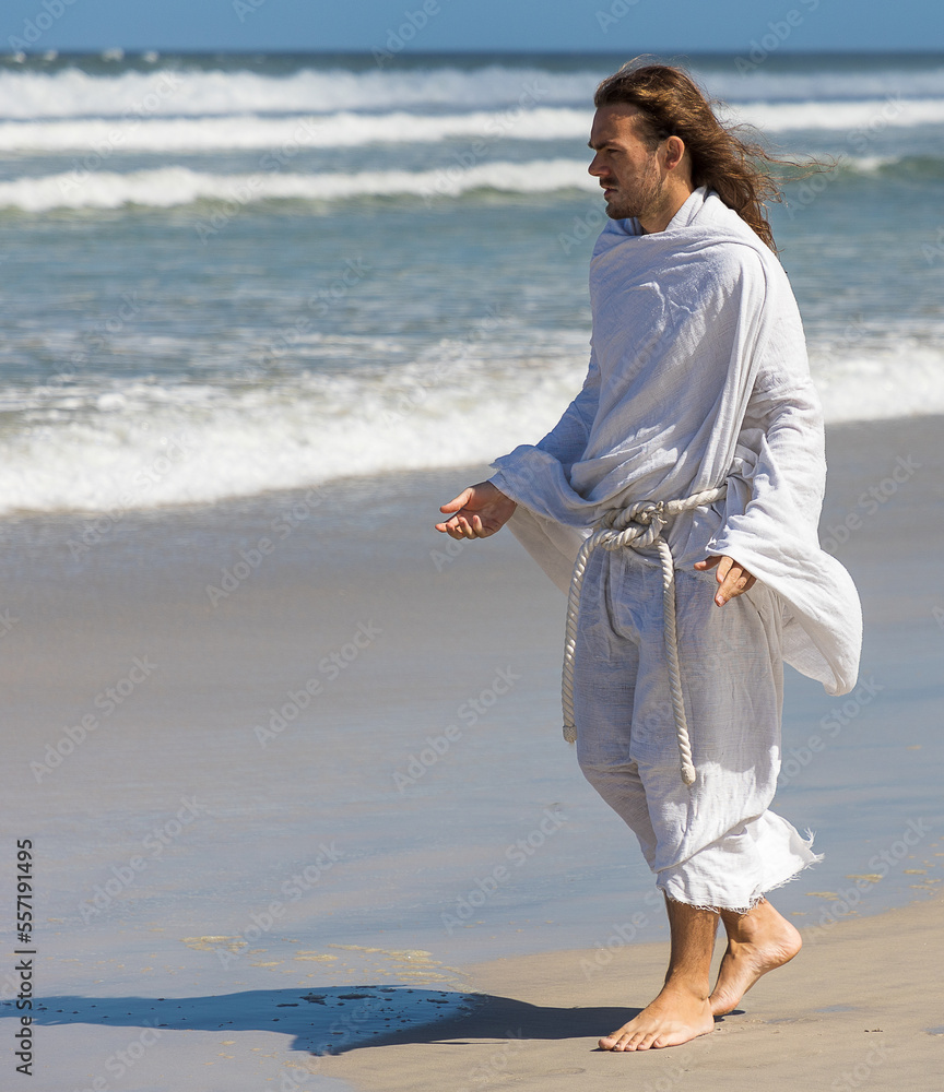 Man in Jesus-type white robes walking on beach with open arms
